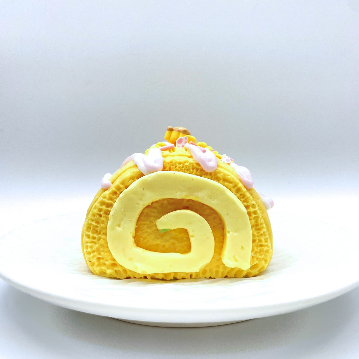 A front-facing view of the Cheese hug taba Squishy, showcasing its soft, yellow, Swiss roll-inspired design with a creamy swirl in the center, perfect for stress relief and relaxation.