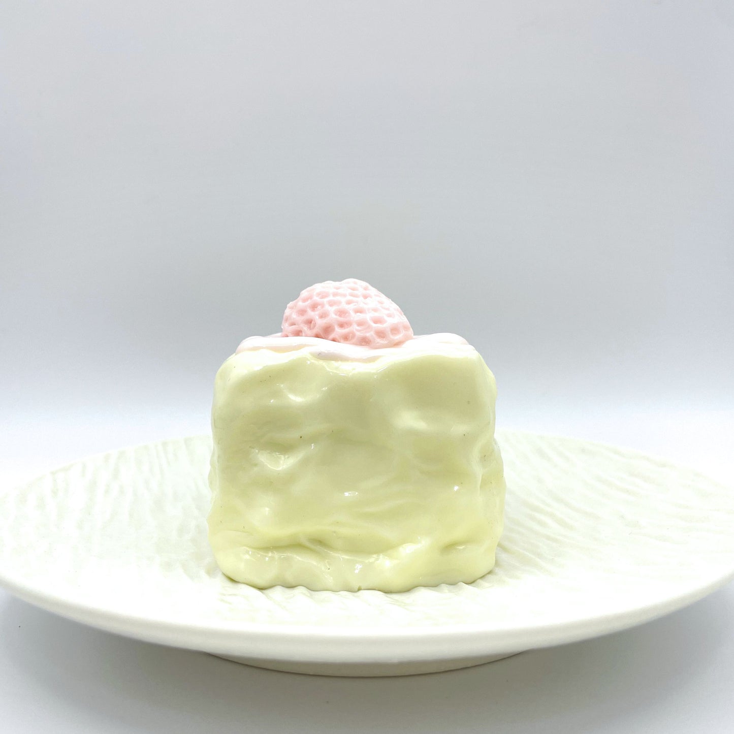 Front view of the Cream Berry Cube Taba Squishy, a soft white cube-shaped stress toy with a strawberry on top