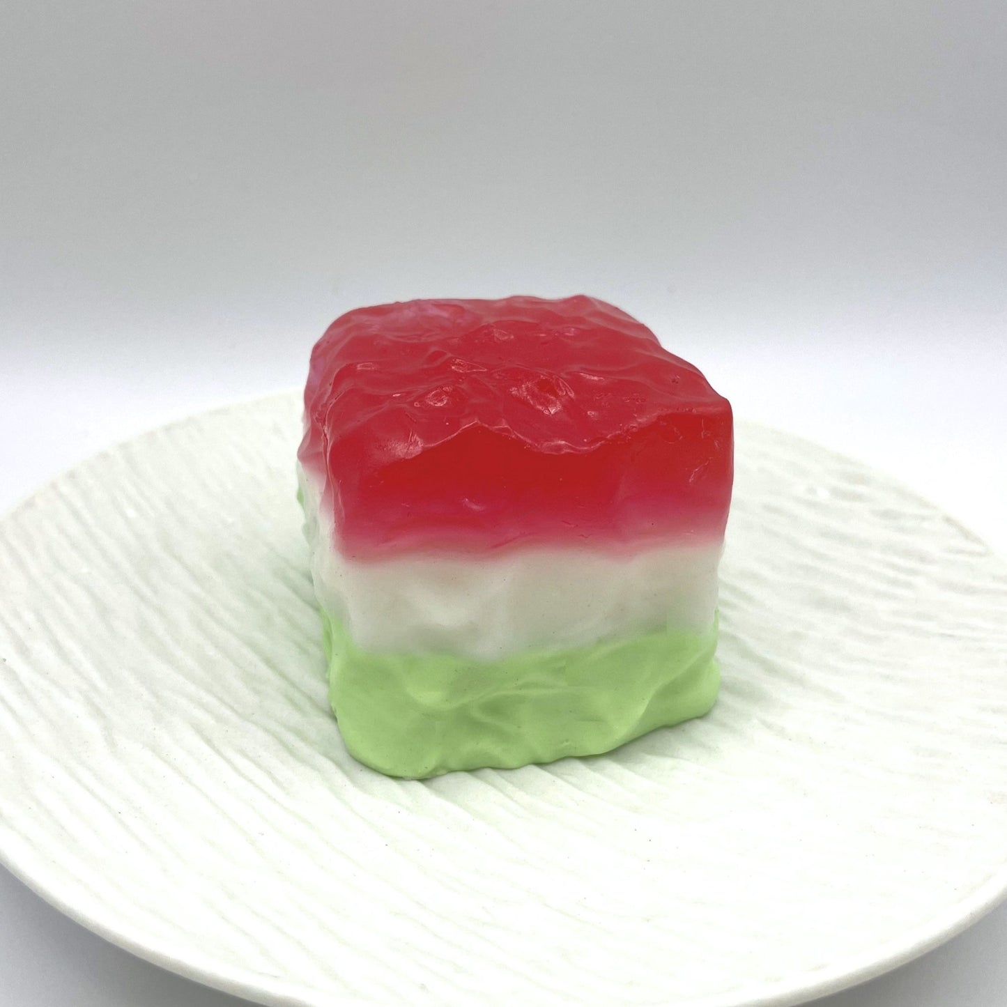 Close-up side view of the Watermelon Cube Taba Squishy, highlighting its jelly-like texture and vivid green-red design